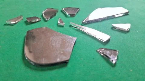 Sharp jagged shards of broken mirror scattered on green background surface Stockfoto's
