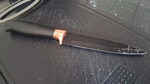 Sharp kitchen knife with black blade and metallic copper bolster Stock Photos