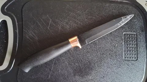 Sharp kitchen knife with black handle resting on textured board Stock Photos