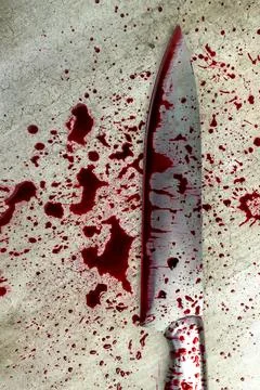 A sharp kitchen knife covered in fresh red blood splatters lying on a grey .. Stock Photos
