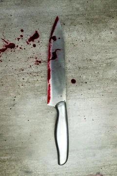 A sharp kitchen knife covered in fresh red blood splatters lying on a grey .. Stock Photos