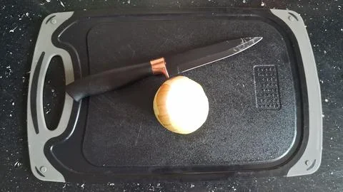 Sharp kitchen knife resting beside a fresh sliced yellow onion piece Stock Photos