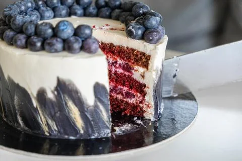 A sharp knife cuts a slice from a round red velvet cake topped with fresh Stock Photos