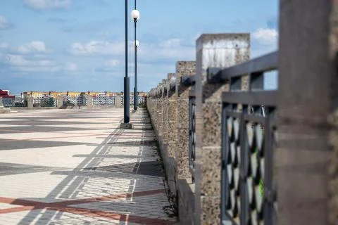 Sharp lines of metal railing fence cast distinct geometric shadows on paved Stock Photos