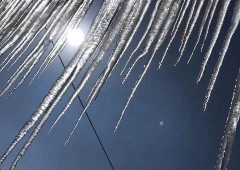 Sharp melting icicles hanging against bright sun and blue sky. 스톡 사진