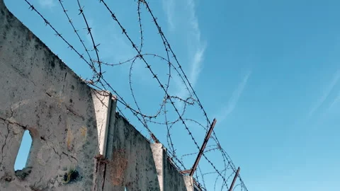 Sharp metal barbed wire along perimeter of high concrete wall separating prison 库存影片 302990563
