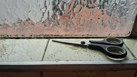 Sharp metal craft scissors resting on a patterned ceramic window sill Stock Photos