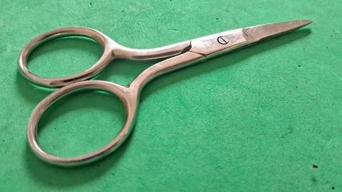 Sharp metal sewing scissors resting on a vibrant green textured surface Stock Photos