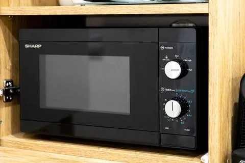 Sharp microwave oven placed on a wooden kitchen shelf with manual control knobs Stock Photos