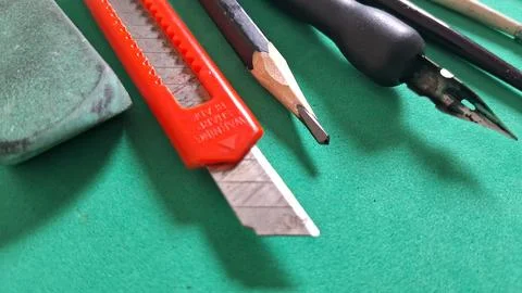 Sharp orange utility knife and pencil resting on green surface Stock Photos