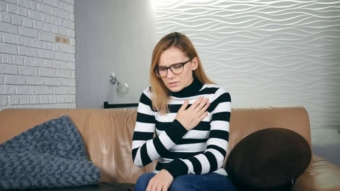 Sharp pain piercing heart of young caucasian woman sitting on sofa, attack of 스톡 동영상 121503900