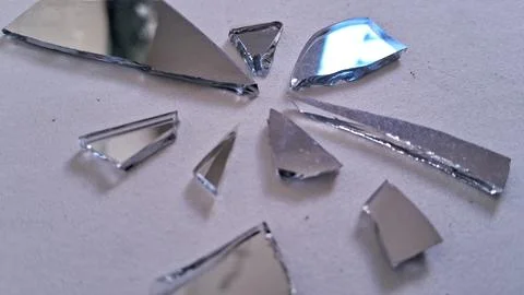 Sharp pieces of broken mirror scattered on a plain white surface Stock Photos