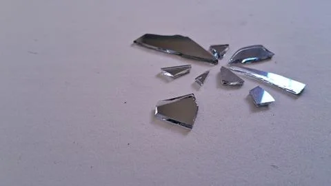 Sharp pieces of a broken mirror scattered on white surface Stock Photos