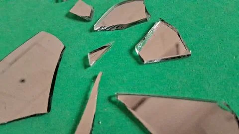 Sharp pieces of broken mirror scattered on a bright green surface Stockfoto's