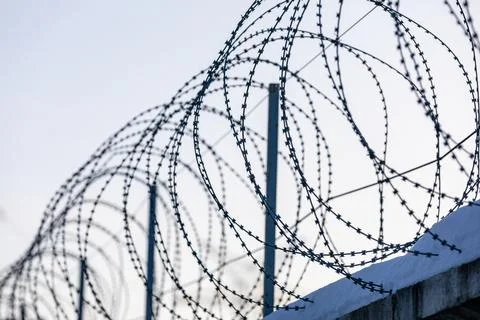 Sharp pointed razor wire barbed fence coiled on top of wall protects from Stock Photos