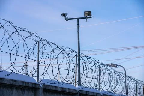 Sharp pointed razor wire barbed fence coiled on top of wall protects from Stock Photos