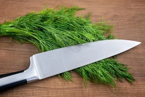 Sharp professional chef knife on a bunch of fresh green dill. Stock Photos