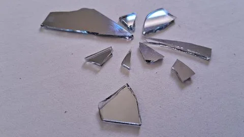 Sharp reflective shards of a broken mirror on white surface floor Stock Photos