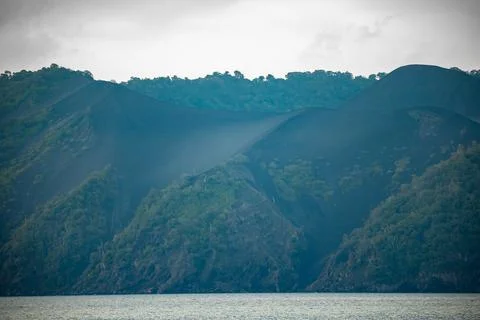 Sharp Ridge of Black Volcanic Ash Slope Meeting Lush Green Tropical Forest Stock Photos