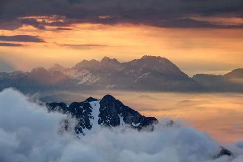 Sharp ridges above sea of clouds illuminated by rising red sun Stock Photos