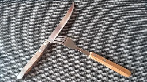 Sharp serrated steak knife and metal fork with wooden handles Stock Photos