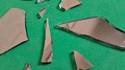 Sharp shards of broken mirror glass scattered on vibrant green background Stockfoto's