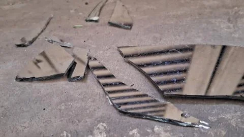 Sharp shards of a broken mirror lying on concrete ground Stock Photos