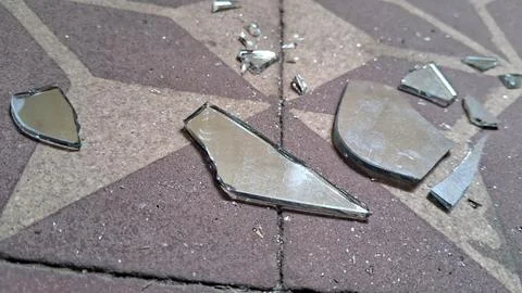 Sharp shards of broken mirror reflecting light on tiled floor surface Stockfoto's