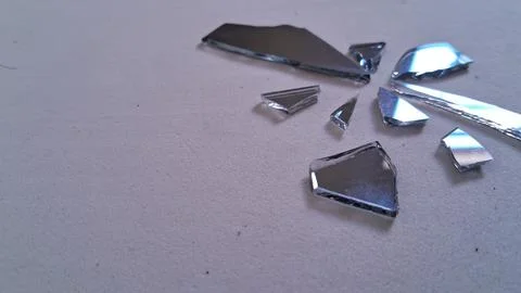 Sharp shards of broken mirror resting on a textured white surface Stock Photos