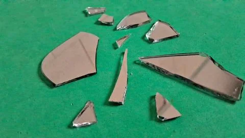 Sharp shards of a broken mirror resting on green paper Stock Photos