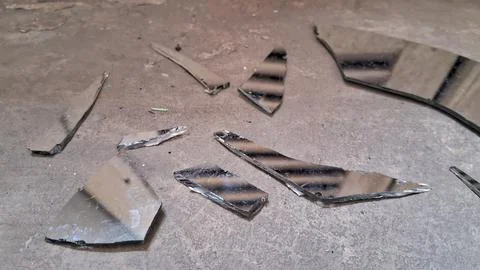 Sharp shards of a broken mirror scattered on concrete floor Stock Photos