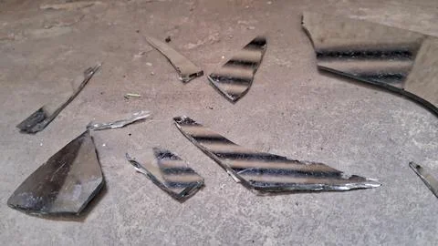 Sharp shards of a broken mirror scattered on concrete floor Stock Photos