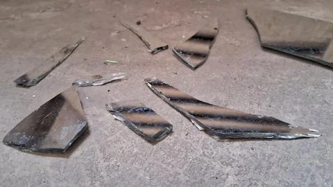 Sharp shards of broken mirror scattered across a rough concrete floor Stock Photos