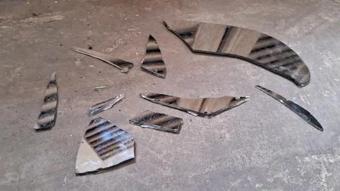 Sharp shards of a broken mirror scattered across concrete floor surface Stock Photos