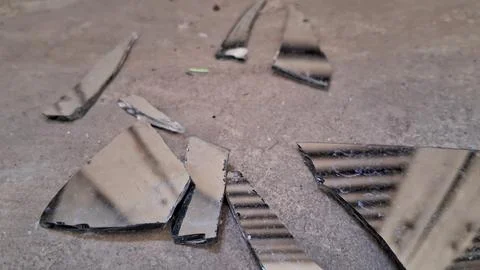 Sharp shards of broken mirror scattered on a gray concrete floor Stock Photos