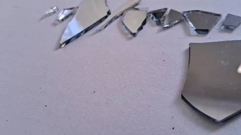 Sharp shards of broken mirror scattered on a plain white surface Stock Photos