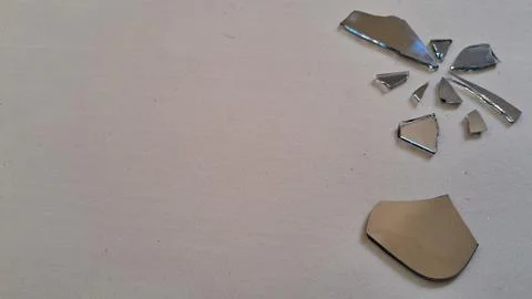 Sharp shards of broken mirror scattered across a plain white surface Stock Photos