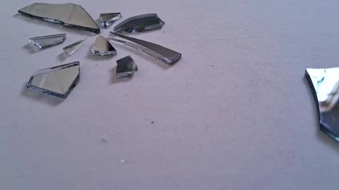 Sharp shards of broken mirror scattered on a plain white surface Stock Photos