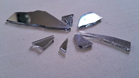 Sharp shards of a broken mirror scattered on white paper Stock Photos