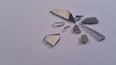Sharp shards of broken mirror scattered on a plain white surface Stock Photos