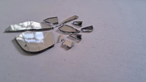 Sharp shards of a broken mirror scattered on white surface Stock Photos