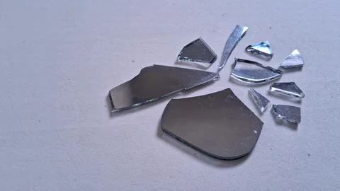 Sharp shards of a broken mirror scattered on white surface Stock Photos