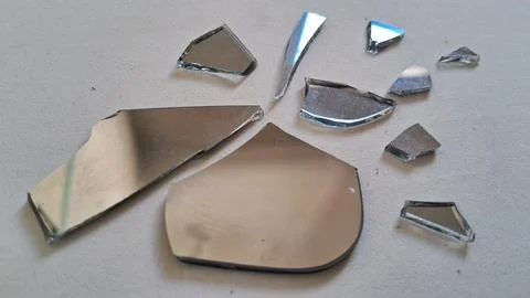 Sharp shards of broken mirror scattered on a plain white surface Stock Photos