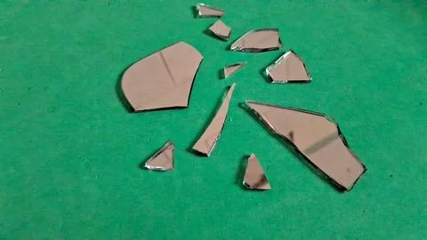 Sharp shards of broken mirror scattered across a vibrant green surface Stockfoto's