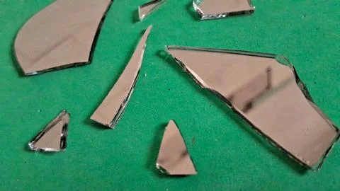 Sharp shards of broken mirror scattered on a bright green surface Stockfoto's