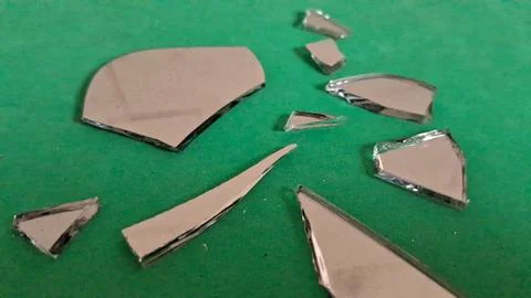 Sharp shards of broken mirror scattered across a vibrant green surface Stockfoto's