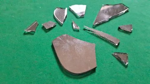 Sharp shards of broken silver mirror scattered on vibrant green surface Stockfoto's