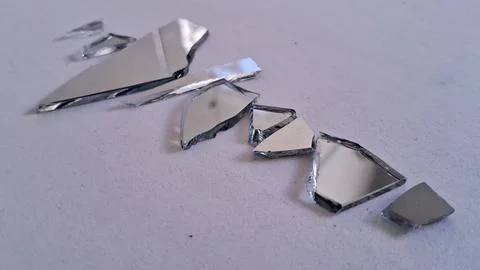 Sharp silver shards of a broken mirror scattered on white surface Stock Photos