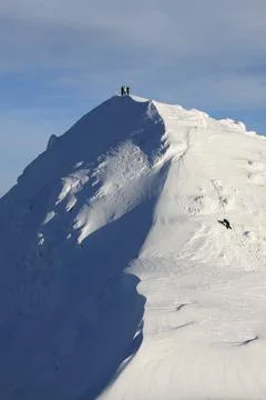 A sharp, snow-covered ridge leading to the summit, on which a few small human Stock-Fotos