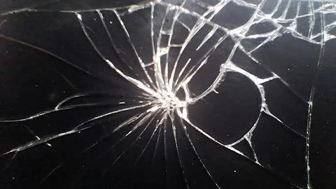 Sharp spiderweb cracks spreading across a dark shattered glass surface Foto stock